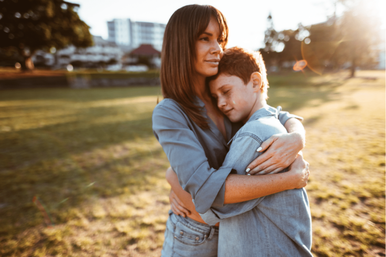 A woman embracing a boy in a sunlit park, providing comfort and reassurance.