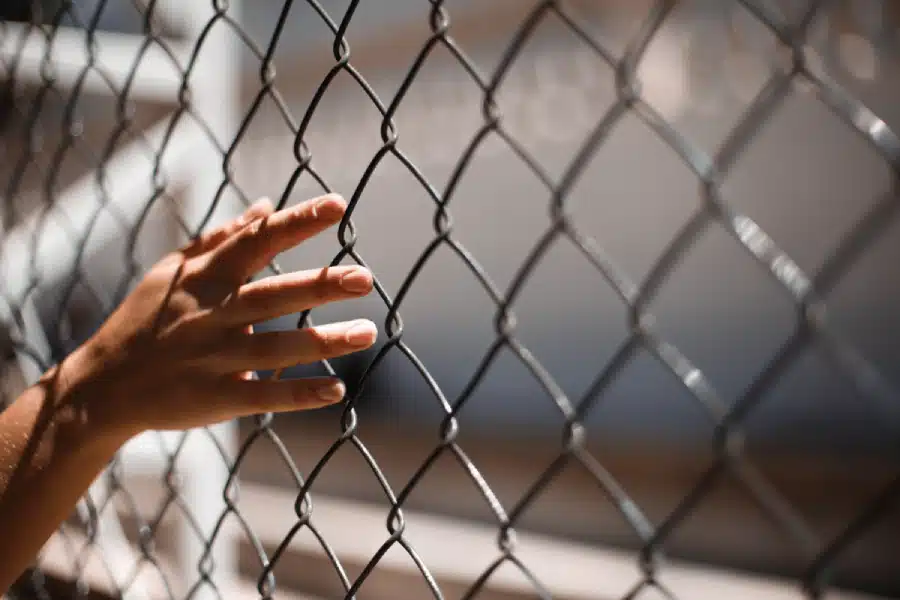 A hand grips a chain-link fence, symbolizing confinement