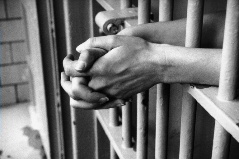 black and photo photo of mans hands through prison bars