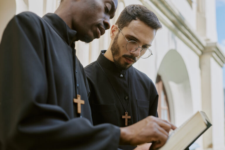 Low angle shot of biracial priests in black robe learning Bible together