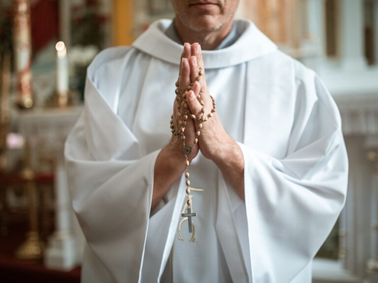 A clergy holding a rosary in prayer inside a church