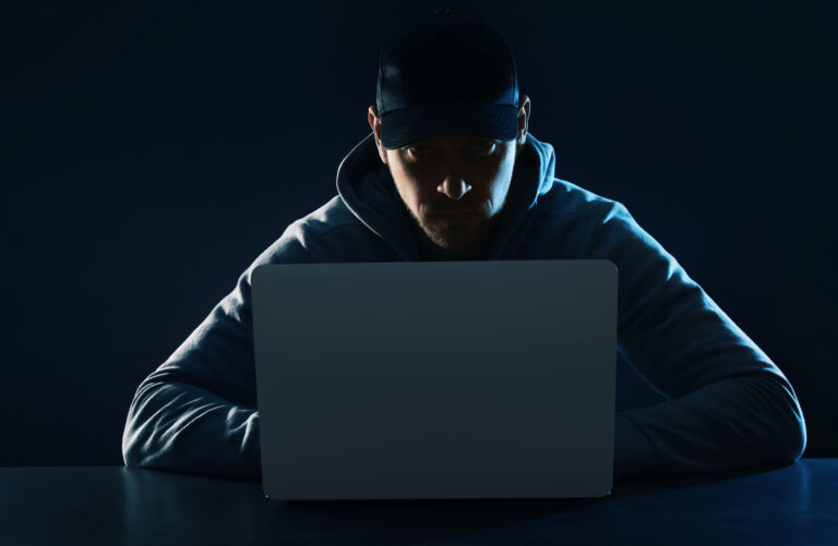 Man in a baseball cap in a room filled with darkness using a computer