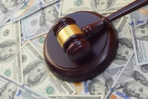 Judge gavel and money on brown wooden table. Many hundred dollar bills under judge malice on court desk from New York clergy sexual abuse settlement.