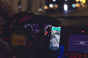 Rideshare driver in a car at night, close-up, view from the car interior, using smartphone to navigate.
