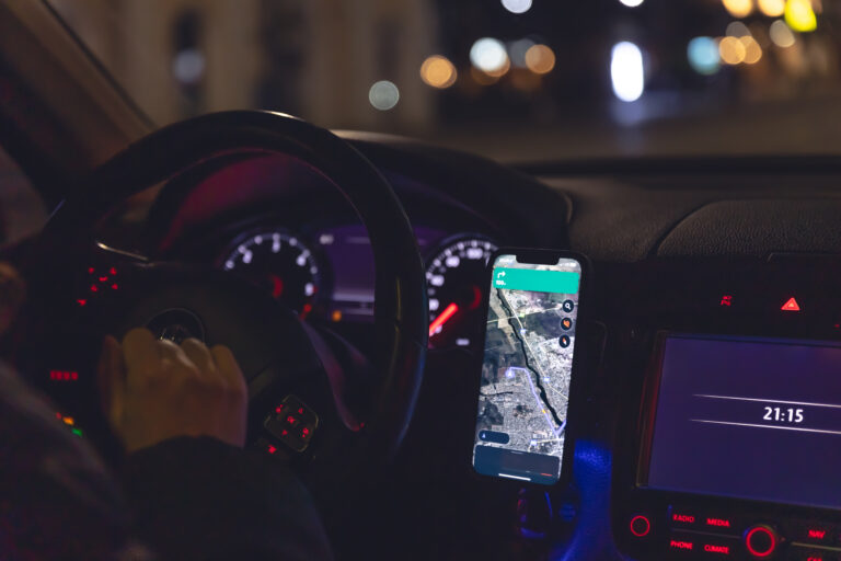 Rideshare driver in a car at night, close-up, view from the car interior, using smartphone to navigate.